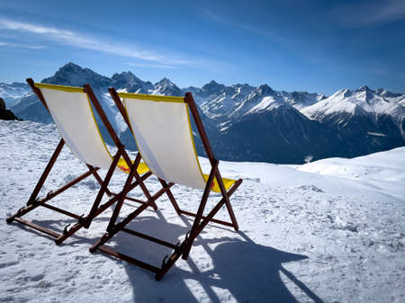 two yellow deck chairs are on the snow and in the background are the mountains of the Alpsの写真素材