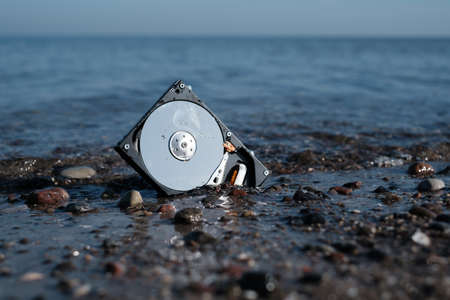 a computer hard disk lies in the shore sand of the sea and is washed by the waterの写真素材