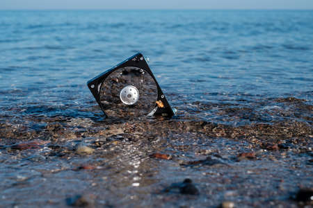 a computer hard disk lies in the shore sand of the sea and is washed by the water