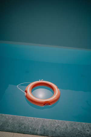 in the blue water of a swimming pool floats a red life ring