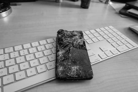 a completely destroyed cell phone lies on a computer keyboard