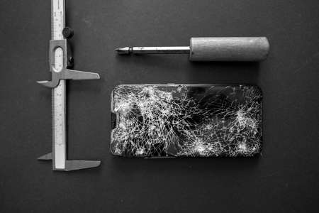 next to a completely destroyed cell phone lies screwdriver and a gaugeの写真素材