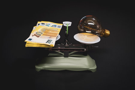 on the scale lies an old light bulb on one side and a bundle of euro banknotes on the other sideの写真素材