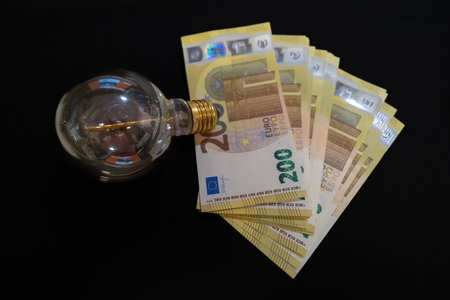 next to an old light bulb is a stack of 200 euro banknotesの写真素材