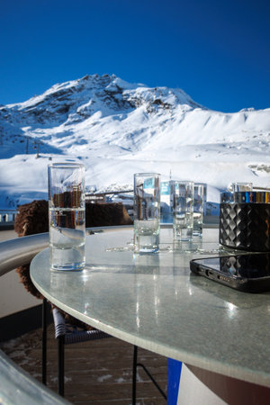 many shot glasses with liquor stand on table in front of snow covered mountainsの写真素材