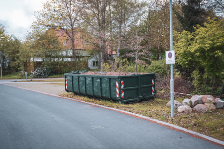 A large green container is completely filled with leaves