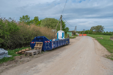 Next to a road is a large blue container for construction waste and a construction site toiletの写真素材