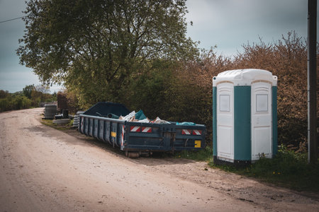 Next to a road is a large blue container for construction waste and a construction site toiletの写真素材