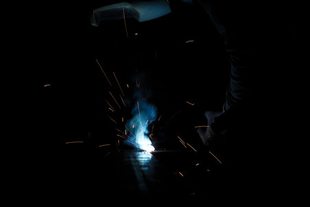 A person wearing a welding mask works on metal with a welding torch, creating sparks through the welding processの写真素材