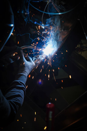 A person wearing a welding mask works on metal with a welding torch, creating sparks through the...