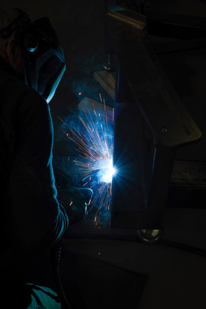 A person wearing a welding mask works on metal with a welding torch, creating sparks through the welding processの写真素材