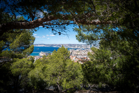 Panoramic view over Marseille, France, with the Old Port (Vieux-Port), Fort Saint-Nicolas, and the Mediterranean Sea under a clear blue sky. The photo captures the vibrant coastal cityscape with historical architecture, modern buildings, and the scenic waterfront. Tourists admire the stunning landscape from a viewpoint near Notre-Dame de la Garde, making this image ideal for travel, tourism, and Mediterranean lifestyle concepts.の写真素材