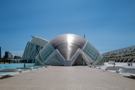 Futuristic architecture of L'HemisfÃ¨ric in the City of Arts and Sciences, Valencia, Spain. The modern building, designed by Santiago Calatrava, resembles a giant eye and is surrounded by reflecting water pools under a clear blue sky. This landmark is a symbol of innovative architecture, cultural tourism, and Mediterranean urban design, making it a popular travel destination in Spain.の写真素材