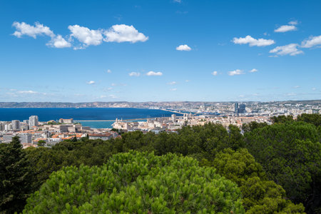 Panoramic view over Marseille, France, with the Old Port (Vieux-Port), Fort Saint-Nicolas, and the Mediterranean Sea under a clear blue sky. The photo captures the vibrant coastal cityscape with historical architecture, modern buildings, and the scenic waterfront. Tourists admire the stunning landscape from a viewpoint near Notre-Dame de la Garde, making this image ideal for travel, tourism, and Mediterranean lifestyle concepts.の写真素材