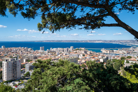 Panoramic view over Marseille, France, with the Old Port (Vieux-Port), Fort Saint-Nicolas, and the Mediterranean Sea under a clear blue sky. The photo captures the vibrant coastal cityscape with historical architecture, modern buildings, and the scenic waterfront. Tourists admire the stunning landscape from a viewpoint near Notre-Dame de la Garde, making this image ideal for travel, tourism, and Mediterranean lifestyle concepts.の写真素材