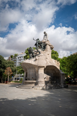 A magnificent monument in Barcelona, Spain, featuring dramatic bronze sculptures atop a grand stone base. The artistic composition depicts expressive human figures symbolizing unity, progress, and freedom. Surrounded by lush trees and urban architecture under a partly cloudy sky, this historical landmark reflects Barcelona's rich cultural heritage and artistic spirit, making it a perfect subject for travel, architecture, and history photography.の写真素材
