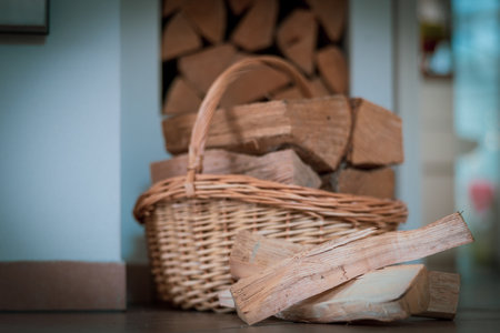 A cozy indoor scene showing a wicker basket filled with neatly stacked firewood next to a wall. The warm tones of the wood and the soft lighting create a comforting, rustic atmosphere, perfect for illustrating home warmth, sustainability, and natural living. Ideal for concepts such as winter preparation, eco-friendly heating, and cozy interior design.の写真素材