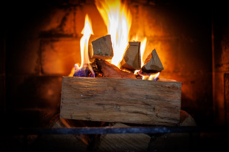A close-up view of a burning fireplace with glowing wooden logs and bright orange flames. The warm fire illuminates the brick interior, creating a cozy and inviting atmosphere. Perfect for illustrating winter comfort, home heating, relaxation, and sustainable living. The detailed shot captures the natural beauty of fire and wood, symbolizing warmth, energy, and homeliness.の写真素材