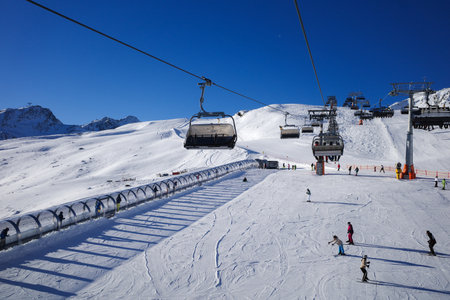 A scenic winter landscape at a modern alpine ski resort featuring chairlifts, skiers, and...