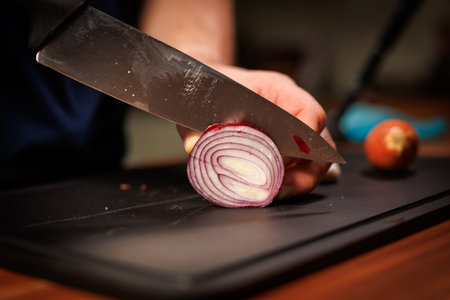 Close-up food photography showing a person slicing a fresh red onion with a sharp kitchen knife on a...