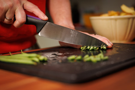 Close-up food photography of a person slicing fresh green beans with a sharp kitchen knife on a...
