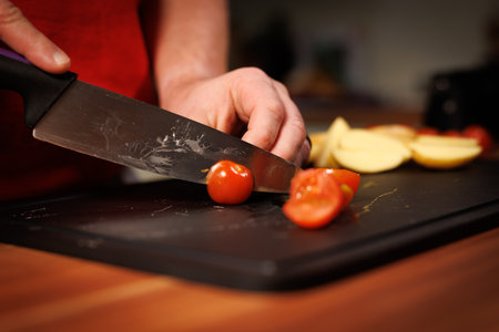 Close-up food photography capturing a person carefully slicing a fresh cherry tomato with a sharp...
