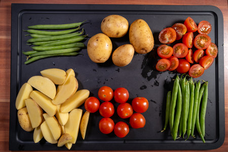 Overhead view of fresh vegetables neatly arranged on a black cutting board, including whole and...