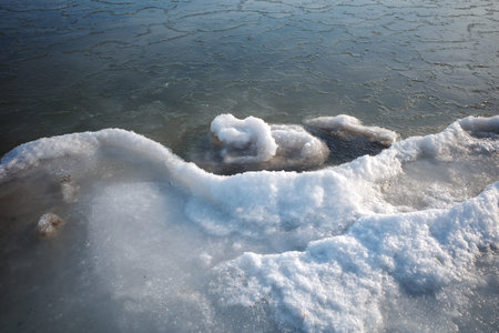 Close-up view of frozen Baltic Sea shoreline with detailed ice formations and snow-covered textures....