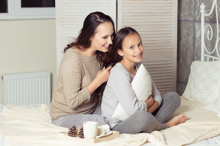Mom and daughter secretive. Mom and daughter resting on the bed. Good morning. Cozy Fall. Winter.の写真素材