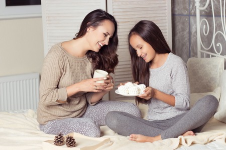 Mom and daughter secretive. Mom and daughter resting on the bed. Good morning. Cozy Fall. Winter.の写真素材