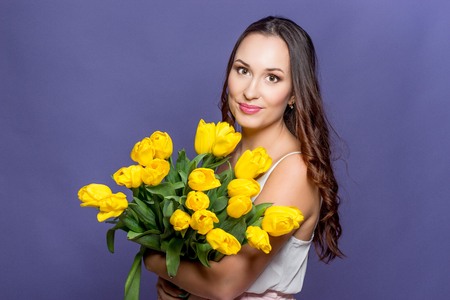 Young beautiful woman holding a bouquet of yellow tulips. Spring.の写真素材