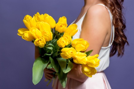 Young beautiful woman holding a bouquet of yellow tulips. Spring.の写真素材