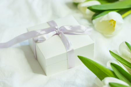 Gift box and a bouquet of white tulips on a bed. Holidays. Spring.の写真素材