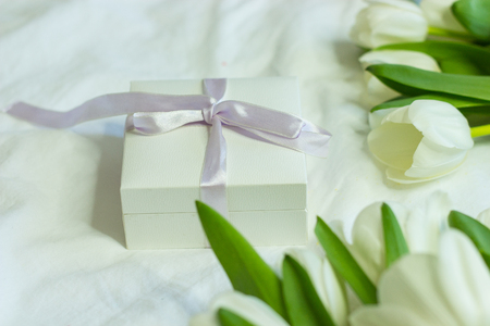 Gift box and a bouquet of white tulips on a bed. Holidays. Spring.の写真素材