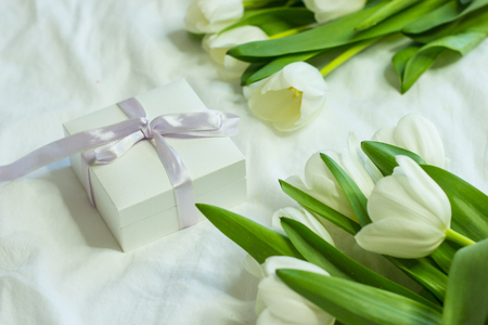 Gift box and a bouquet of white tulips on a bed. Holidays. Spring.