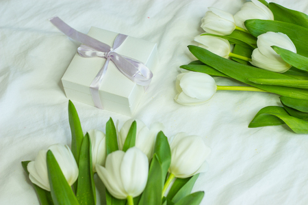 Gift box and a bouquet of white tulips on a bed. Holidays. Spring.の写真素材