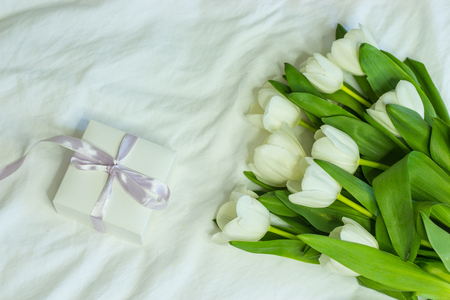 Gift box and a bouquet of white tulips on a bed. Holidays. Spring.の写真素材