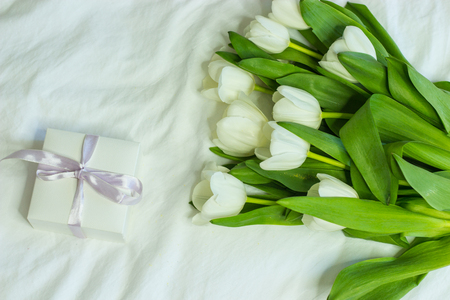 Gift box and a bouquet of white tulips on a bed. Holidays. Spring.の写真素材