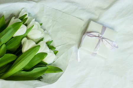 Gift box and a bouquet of white tulips on a bed. Holidays. Spring.の写真素材