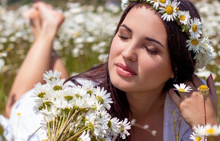 Portrait of a beautiful young woman in chamomile field. Happy girl collecting daisies. A girl resting in a field of chamomile. Spring.の写真素材