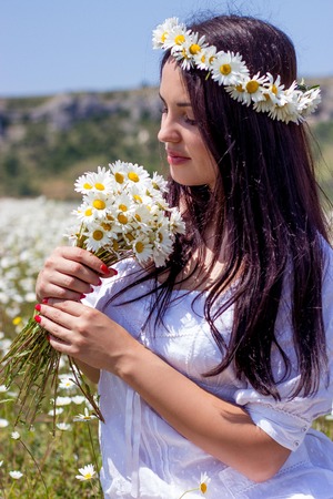 Portrait of a beautiful young woman in chamomile field. Happy girl collecting daisies. A girl resting in a field of chamomile. Spring.の写真素材
