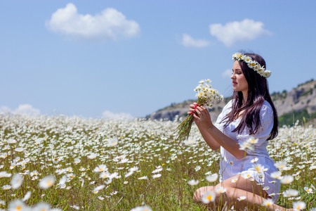 Portrait of a beautiful young woman in chamomile field. Happy girl collecting daisies. A girl resting in a field of chamomile. Spring.の写真素材