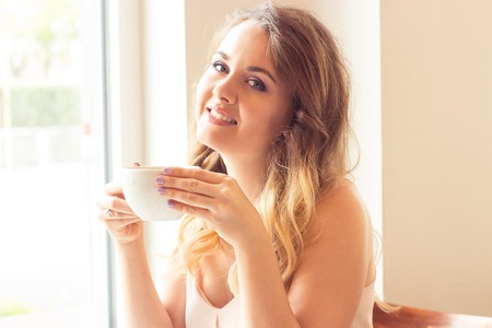 A beautiful young woman sitting in a cafe. Girl drinks Cappuccino.の写真素材