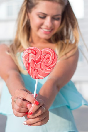 Girl holding a lollipop. Beautiful happy blond girl in the street. Young woman eating a piece of candy.の写真素材