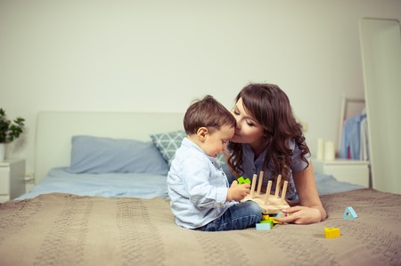 Young mom and young son sitting on the bed. Mom plays with her son. Family.の写真素材