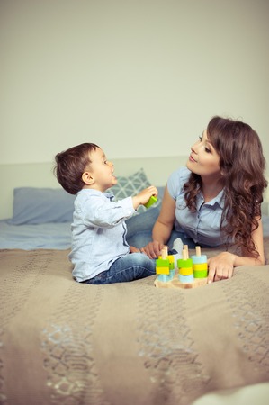 Young mom and young son sitting on the bed. Mom plays with her son. Family.の写真素材