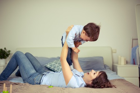 Young mom and young son sitting on the bed. Mom plays with her son. Family.の写真素材