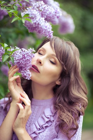 Young beautiful woman walks along the spring garden. A girl stands near the lilacs. Lilac. Flowers.の写真素材