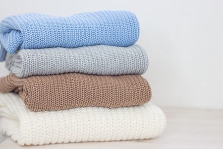 A pile of warm autumn clothing on a wooden shelf. Sweaters. Knitted winter wear. Cozy.の写真素材