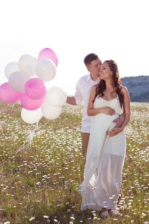 Portrait of a family in the chamomile field. Pregnant woman holds beads. Family with balloons.の写真素材